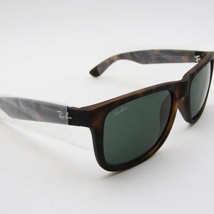 Puede incluir: Gafas de sol marrones y negras con lentes verdes. Las gafas tienen una montura rectangular y un patr&oacute;n de carey en las patillas. El logotipo de Ray-Ban es visible en la lente y la patilla.