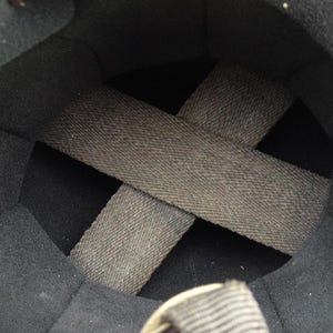 May include: Interior view of a black helmet. The inside is lined with dark gray fabric and features a crisscross pattern of gray straps for support and fit. The helmet's interior is designed for protection and comfort.