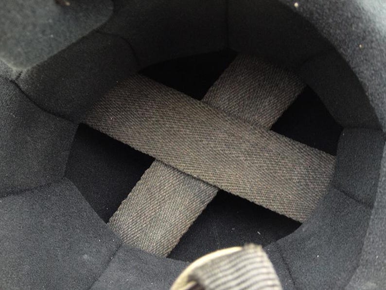 May include: Interior view of a black helmet. The inside is lined with dark gray fabric and features a crisscross pattern of gray straps for support and fit. The helmet's interior is designed for protection and comfort.