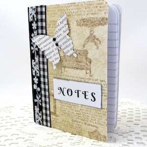 Puede incluir: Un pequeño cuaderno a cuadros blanco y negro con un diseño decorativo de mariposa y la palabra "NOTES" en la portada.