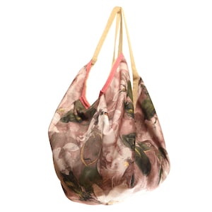 Può includere: Una borsa tote con stampa floreale rosa e verde, bordatura rosa e manici beige.