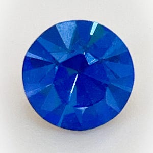 May include: A single, round, blue rhinestone with a faceted design.