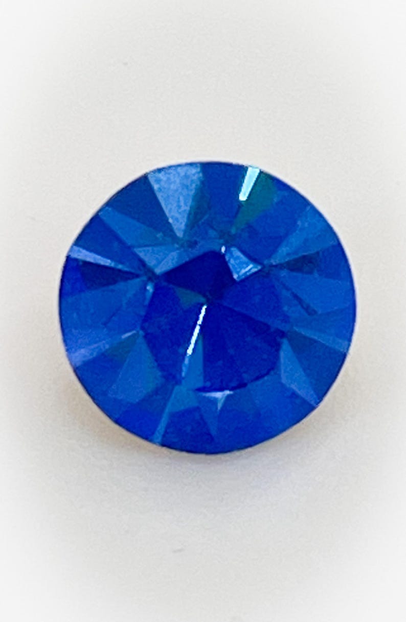 May include: A single, round, blue rhinestone with a faceted design.