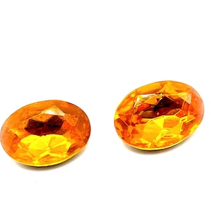 May include: Two orange oval-shaped rhinestones with a faceted design.
