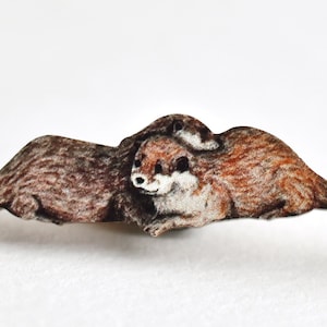 May include: A hand-painted illustration of two otters, one on top of the other, with their tails outstretched. The otters are brown and white with a realistic style.