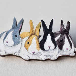 May include: Four wooden rabbit figurines painted in different colors. The rabbits are black and white, gray and white, brown and white, and yellow and white. The rabbits are all facing forward and are arranged in a row.