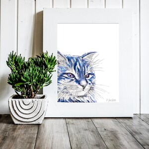 Puede incluir: Una pintura de acuarela enmarcada de un gato azul y blanco con ojos morados. El gato est&aacute; mirando hacia la derecha del marco. La pintura est&aacute; sobre un fondo blanco y tiene un marco blanco.