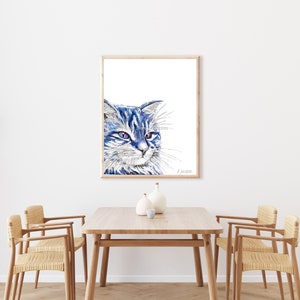 Puede incluir: Una pintura de acuarela de un gato azul con ojos verdes, enmarcada en un marco de madera clara. El gato est&aacute; mirando hacia la derecha de la imagen.