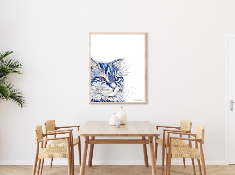 Puede incluir: Una pintura de acuarela de un gato azul con ojos verdes, enmarcada en un marco de madera clara. El gato est&aacute; mirando hacia la derecha de la imagen.