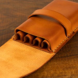 Leather pencil case in sadle tan , with compartments for 4 pens lying on a wooden board