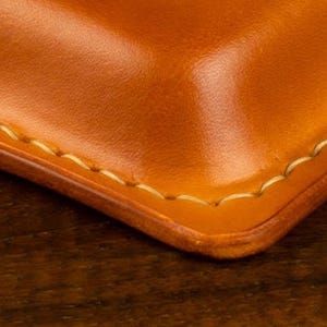 Leather pencil case in sadle tan , with compartments for 4 pens lying on a wooden board