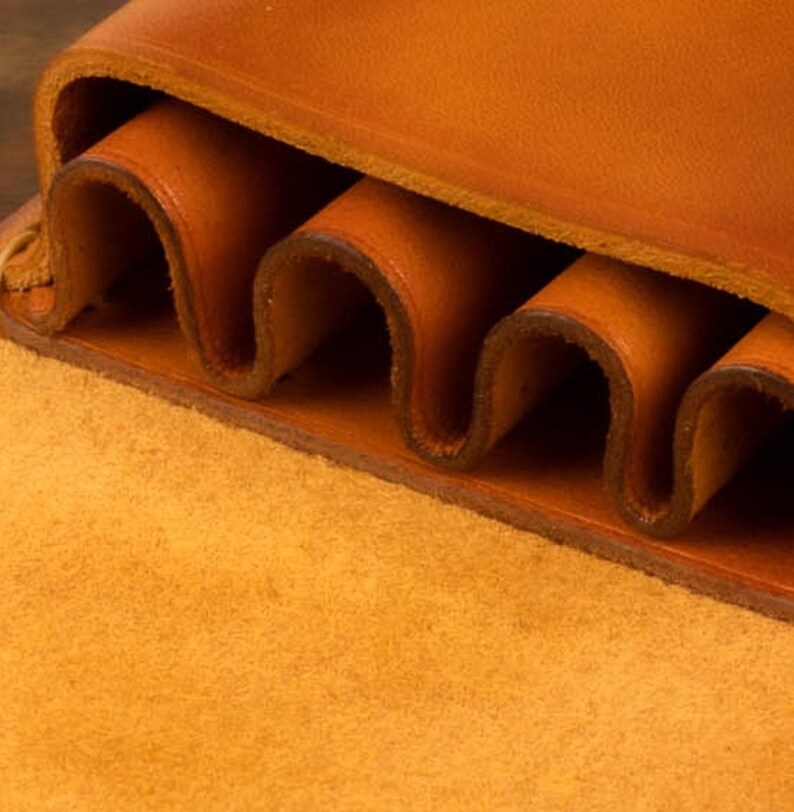 Leather pencil case in sadle tan , with compartments for 4 pens lying on a wooden board