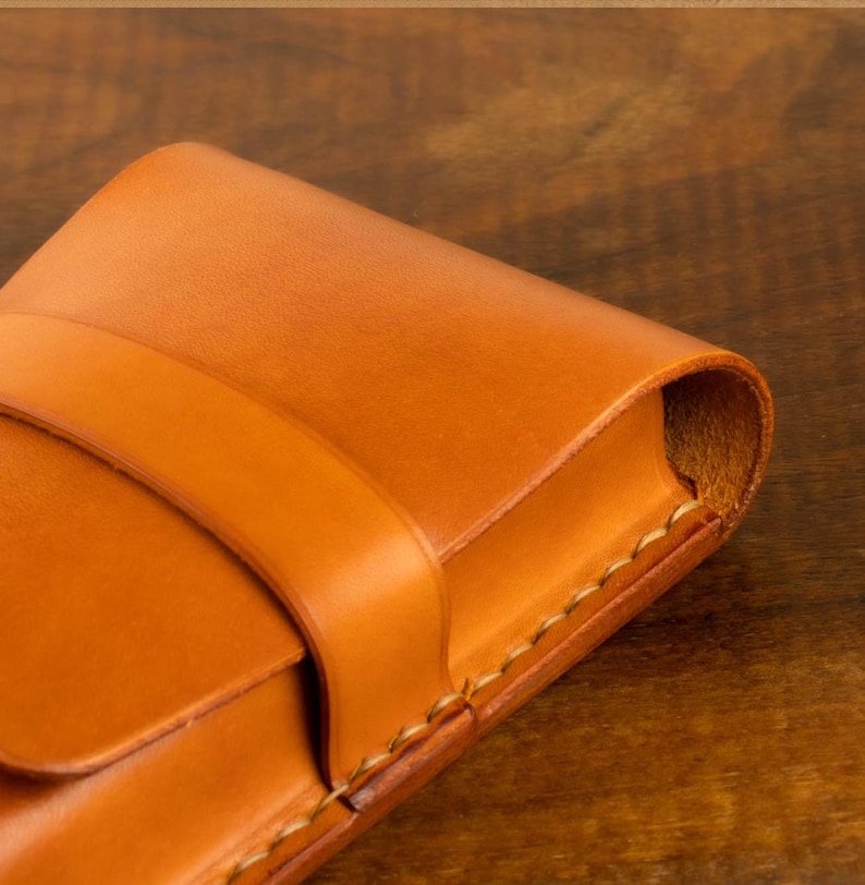 Leather pencil case in sadle tan , with compartments for 4 pens lying on a wooden board
