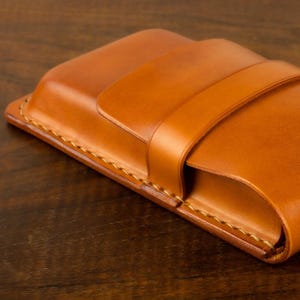 Leather pencil case in sadle tan , with compartments for 4 pens lying on a wooden board