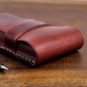 Leather pencil case with compartment in mahogany color lying on a wooden board