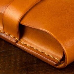 Leather pencil case in sadle tan , with compartments for 4 pens lying on a wooden board