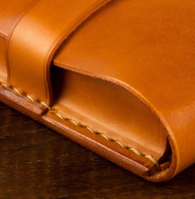 Leather pencil case in sadle tan , with compartments for 4 pens lying on a wooden board