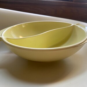 May include: A yellow divided serving bowl with a handle. The bowl is made of plastic and has a smooth, glossy finish.