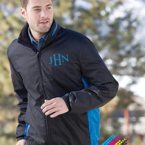 May include: Black and blue jacket with the initials "JHN" embroidered in blue. The jacket has a zipper closure, blue accents on the sides and collar, and elastic cuffs. The jacket is worn over a denim shirt.