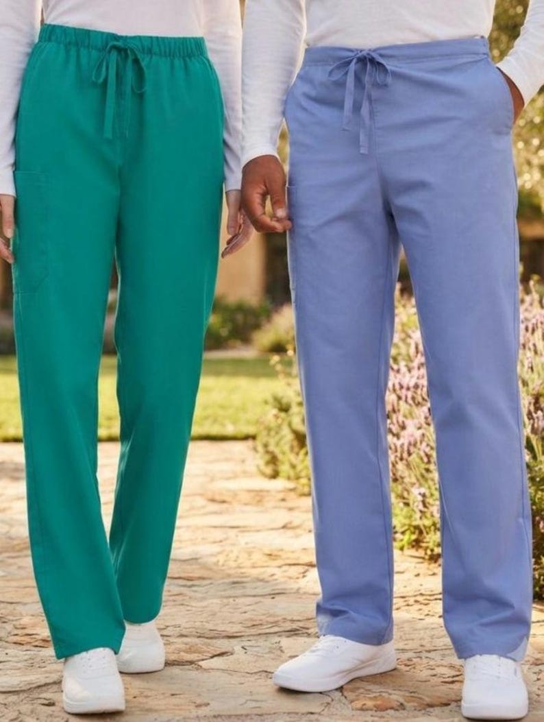 May include: Two pairs of scrub pants, one in solid teal and one in solid light blue. Both pairs feature an elastic waistband with a matching drawstring tie, straight legs, and side pockets, paired with white sneakers and long-sleeved white shirts.