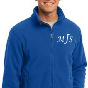 May include: Royal blue fleece jacket with a full zip and side pockets. The jacket features the white initials "MJs" on the upper left chest. The model is wearing a grey undershirt.