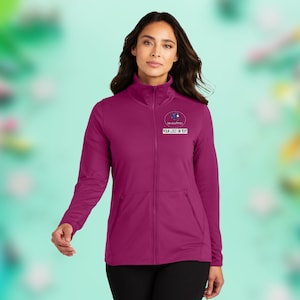 May include: A magenta full-zip jacket with a mock neck collar. The jacket features a small logo and the text "YOUR LOGO OR TEXT" on the chest. The jacket has two front pockets and is made of a smooth, athletic material.
