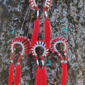 May include: Four red and white beaded dreamcatchers with red feathers hanging from a tree trunk.