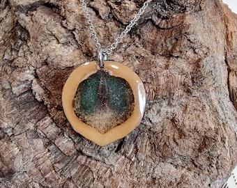 May include: A silver chain necklace with a round pendant made of light brown ceramic with a green and brown design inside.