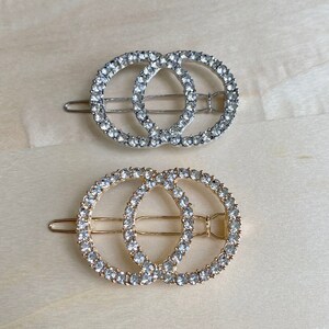 May include: Two interlocking circle hair clips, one silver and one gold, both adorned with clear rhinestones.