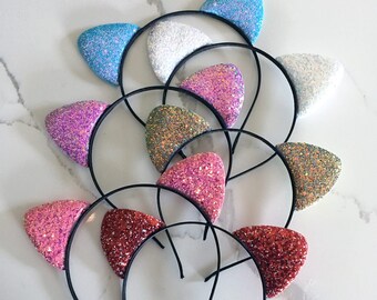 May include: A set of ten colorful glitter cat ear headbands. Each headband features a different color of glitter, including pink, blue, red, and gold. The headbands are perfect for adding a touch of fun to any outfit.