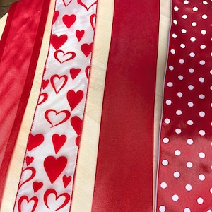 Könnte beinhalten: Vier rote Bandspulen mit verschiedenen Mustern. Die erste Spule ist ein einfarbiges rotes Band. Die zweite Spule hat einen weißen Hintergrund mit roten Herzen. Die dritte Spule ist ein einfarbiges rotes Band. Die vierte Spule hat einen roten Hintergrund mit weißen Punkten.