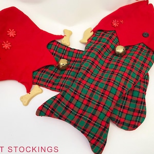 May include: Two pet stockings shaped like fish. One is red with snowflake accents and bone-shaped ornaments. The other is red and green plaid with gold bells and bone-shaped ornaments. The text "PET STOCKINGS" is at the bottom.