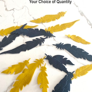 Op de afbeelding: Een verzameling van viltveren in twee kleuren: mosterdgeel en donkergrijs. De veren zijn verspreid over een wit marmeren oppervlak.  "Your Choice of Color" en "Your Choice of Quantity" staan in zwarte tekst bovenaan de afbeelding.