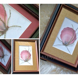 May include: A framed pressed flower art piece with a pink seashell and green stems. The frame is brown with a black outer edge. The background is white.