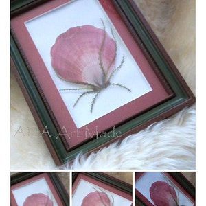 May include: A framed pressed flower art piece with a pink flower in a green and brown frame.