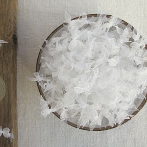 May include: A bowl filled with white tulle bows. The tulle is soft and delicate, and the bows are arranged in a random pattern.