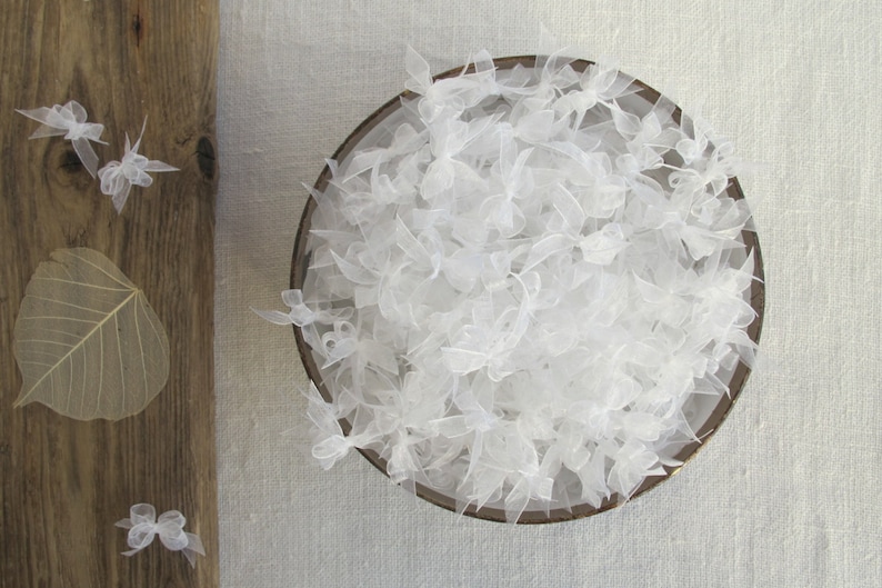 May include: A bowl filled with white tulle bows. The tulle is soft and delicate, and the bows are arranged in a random pattern.