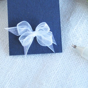 May include: A white tulle bow tied on a dark blue card.