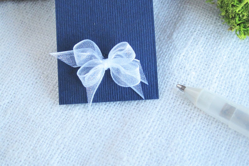 May include: A white tulle bow tied on a dark blue card.