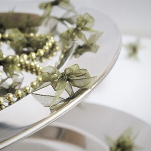 May include: A silver platter with a gold beaded garland and green ribbon bows. The platter is on a white surface.
