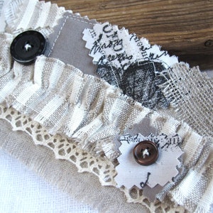 Könnte beinhalten: Ein handgefertigtes Armband aus Stoff mit einem mehrschichtigen Design aus Spitze, Sackleinen und bedrucktem Stoff. Das Armband hat zwei Knöpfe, einen schwarzen und einen braunen.