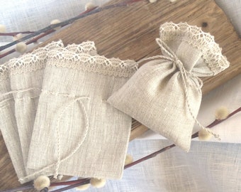 May include: Set of four small, natural linen drawstring bags with delicate white lace trim. The bags are tied with twine and are displayed on a wooden surface.