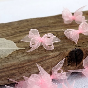 Op de afbeelding: Een verzameling kleine roze tule strikjes, verspreid over een houten oppervlak. De strikjes zijn gemaakt van delicate, doorschijnende stof en hebben een zachte, vrouwelijke uitstraling.