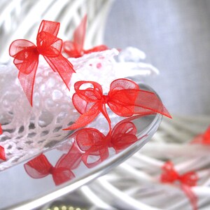 May include: A white crocheted doily with red bows on a silver tray. The doily is on top of a white wicker wreath.