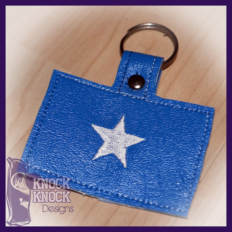 May include: A blue leather keychain with a white star and a silver key ring. The keychain has the text "Knock Knock Designs" on it.