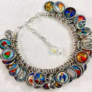 May include: A silver charm bracelet with a variety of religious medallions and charms. The charms feature images of saints, the Virgin Mary, and other religious symbols. The bracelet is made of a silver chain and has a lobster clasp closure.
