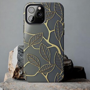May include: A gray phone case with a gold leaf design. The case has a raised camera bump with three lenses.