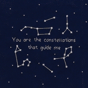 May include: A navy blue background with white embroidered stars forming constellations. The text "You are the constellations that guide me" is embroidered in white.
