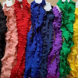 May include: A collection of ruffled fabric trim in various colors, including white, black, pink, red, blue, purple, green, and yellow. Each trim piece is attached to a white tag. The trim has a wavy, textured edge.