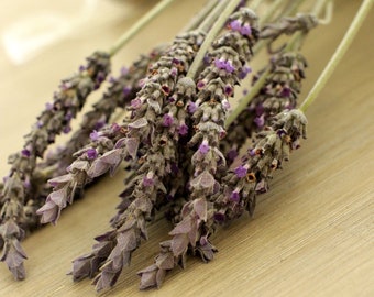 May include: A bunch of dried lavender flowers with purple blooms. The lavender is arranged on a light brown wooden surface.